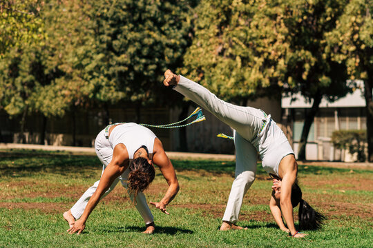 mujeres practicando patadas, ejercicios y capoeira en la ciudad con su ropa de capoeira en un parque verde en un d&iacute;a soleado.