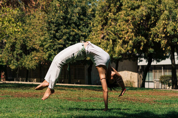 mujer morena con ropa de capoeira practicando y flexionando su cuerpo en un parque de la ciudad.	