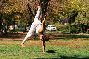 mujer morena brasilera practicando capoeira flexionando y girando su cuerpo en la naturaleza en un...