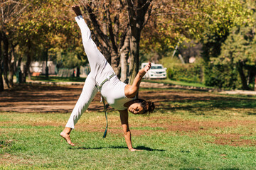 mujer morena brasilera practicando capoeira flexionando y girando su cuerpo en la naturaleza en un...