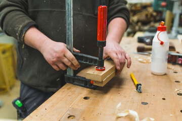 Closeup shot of unrecognizable male carpenter using bar clamp to glue two wood pieces together....