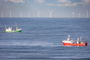 Two cutters passing each other in the North sea with wind turbines of a windfarm in the background