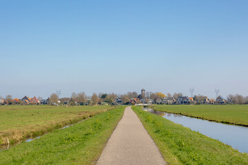 Fototapeta na wymiar Spring countryside landscape, Flat, low and water land, Typical Dutch polder with canal or ditch on the green meadow field, Small villages and church tower under blue sky in North Holland, Netherlands