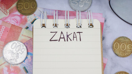 ZAKAT words handwritten in a notebook, Indonesia Money Rupiah, and coins. Ramadan Concept