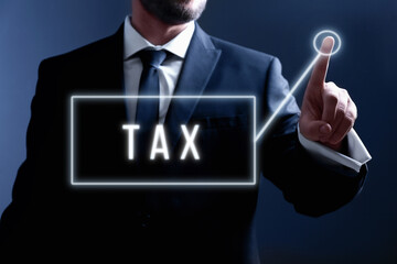 Businessman using virtual screen with word TAX on dark background