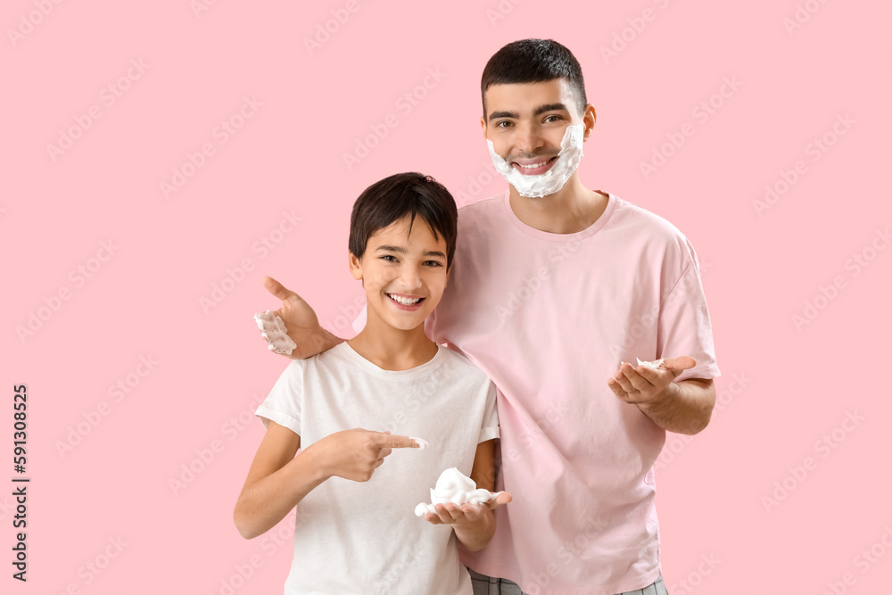 Poster Man and his little son applying shaving foam onto faces against pink background