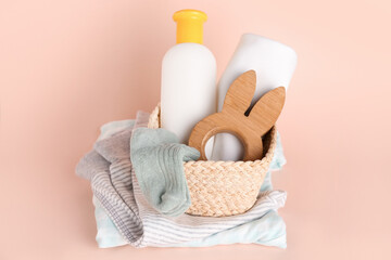 Fototapeta na wymiar Basket with wooden toy, bottle of cosmetic product and baby clothes on color background