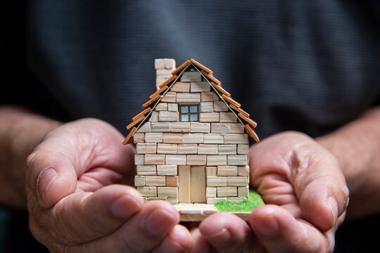Manos que sostienen una casa en miniatura hecha de ladrillos