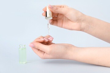 Woman applying oil onto cuticles on light background