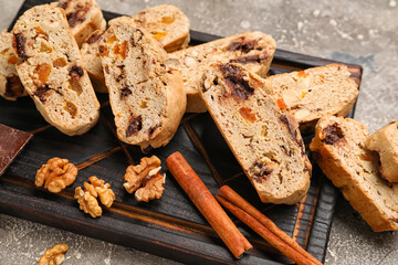 Wooden board with tasty biscotti cookies, walnuts and cinnamon on grunge background, closeup