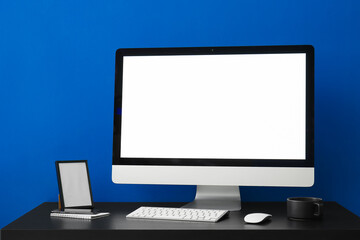 Workplace with computer, frame and cup near blue wall