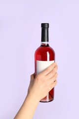 Female hand holding bottle of red wine on lilac background