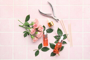 Composition with bottles of cuticle oil, manicure instruments and rose flowers on color tile background