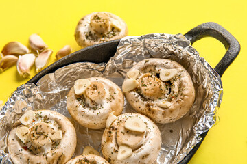 Baking dish with raw mushrooms, spices and garlic on yellow background, closeup