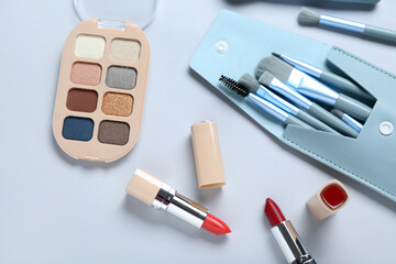 Beautiful lipsticks, eyeshadows and makeup brushes on light background