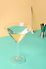 Glass of martini, bar spoon and jigger on color background