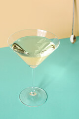 Glass of martini, bar spoon and jigger on color background