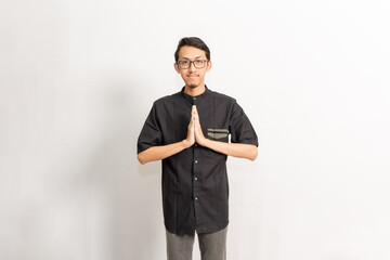 A man wearing a black shirt and glasses give a warm greeting. Indonesian or southeast asian model with black t-shirt and folded sarong isolated in front of white background.