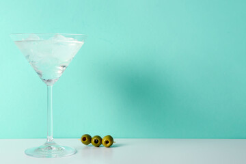 Glass of martini with olives and ice on color background