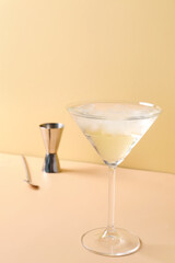 Glass of martini with ice, bar spoon and jigger on beige background