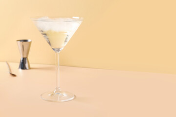 Glass of martini with ice, bar spoon and jigger on beige background