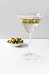 Glass of martini and olives on light background