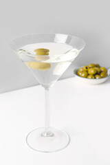 Glass of martini and olives on light background