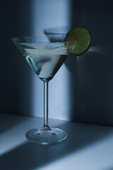 Glass of martini with lime on blue background