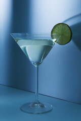 Glass of martini with lime on blue background