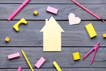 Paper house with school stationery and toys on dark wooden background. Children's Day celebration