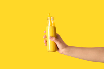 Female hand with glass bottle of yellow smoothie on color background