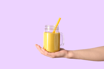 Female hand with Mason jar of yellow smoothie on pink background