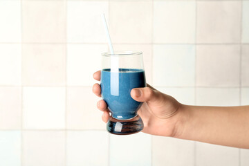 Female hand with glass of blue smoothie on white background