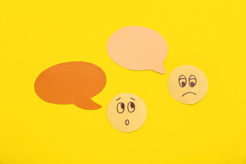 Paper faces with speech bubbles on yellow background. Dialogue concept