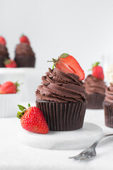 Chocolate cupcake with dark chocolate buttercream and strawberries, double chocolate cupcakes with american buttercream, tall swirl frosting on a cupcake with a strawberry
