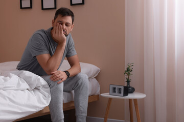 Sleepy man sitting on bed at home