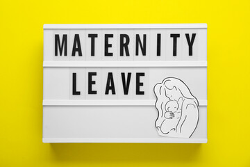 Maternity leave concept. Lightbox with paper cutout of mother and child on yellow background, top view