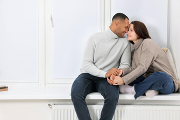 Dating agency. Happy couple holding hands and sitting on window sill at home, space for text