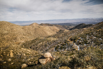 Far view of dirt trail cutting across grassy rolling hills in Arizona desert near Kingman in Hualapai mountains with patches of snow