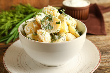 Bowl of tasty Potato Salad with greens on wooden background, closeup