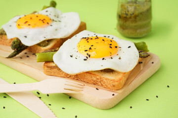 Delicious sandwiches with fried eggs and asparagus on green background