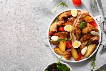 Plate of tasty potato salad with eggs, tomatoes and bacon on light background, top view