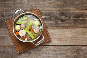 Fototapeta na wymiar Different ingredients for cooking tasty bouillon in pot on wooden table, top view. Space for text