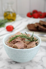 Bowl with canned tuna and rosemary on white marble table, closeup