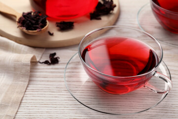 Fresh hibiscus tea and dry flower leaves on wooden table, closeup