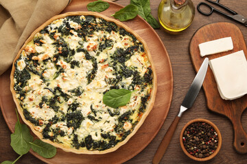 Delicious homemade spinach quiche, spices and knife on wooden table, flat lay
