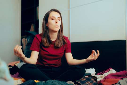 Calm Woman Sitting in Yoga Pose on a Pile of Clothes. Professional organizer taking a deep breath before cleaning a closet
