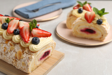 Tasty meringue roll with jam, cream, strawberry, blueberry and mint on light grey marble table, closeup