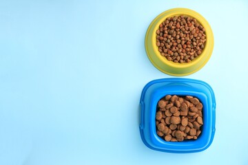 Dry pet food in feeding bowls on light blue background, flat lay. Space for text