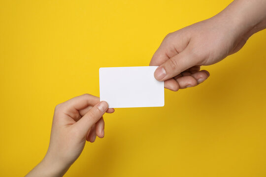 Man and woman holding blank gift card on yellow background, closeup
